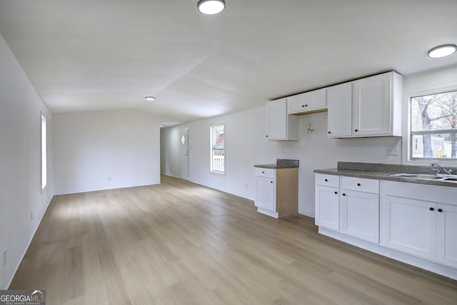 kitchen with lofted ceiling, sink, white cabinetry, light hardwood / wood-style flooring, and a wealth of natural light