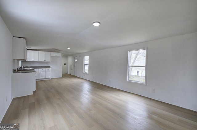 unfurnished living room with sink, vaulted ceiling, and light hardwood / wood-style floors