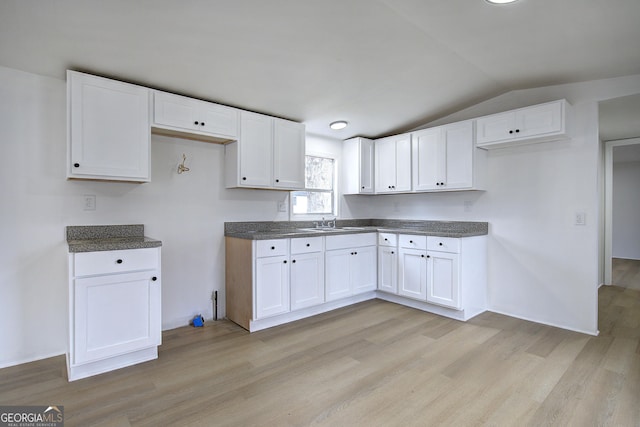 kitchen featuring white cabinetry, vaulted ceiling, sink, and light hardwood / wood-style floors