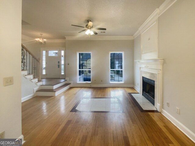 unfurnished living room featuring a high end fireplace, ceiling fan with notable chandelier, light hardwood / wood-style flooring, and a wealth of natural light