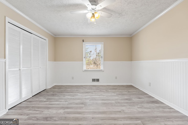 unfurnished bedroom with a textured ceiling, ornamental molding, a closet, ceiling fan, and light hardwood / wood-style floors