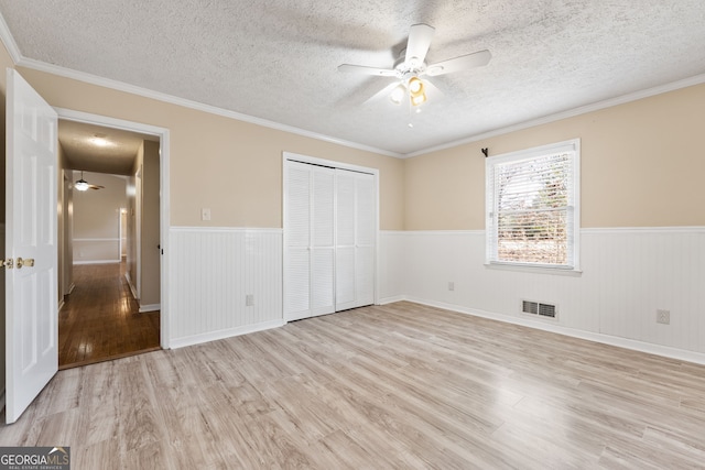 unfurnished bedroom featuring crown molding, a textured ceiling, light wood-type flooring, a closet, and ceiling fan