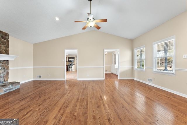 unfurnished living room featuring vaulted ceiling, a stone fireplace, hardwood / wood-style floors, and ceiling fan