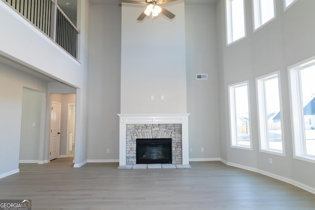 unfurnished living room featuring a stone fireplace, wood finished floors, visible vents, and a healthy amount of sunlight