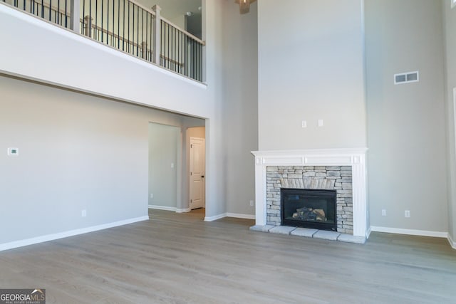 unfurnished living room with baseboards, visible vents, wood finished floors, and a stone fireplace