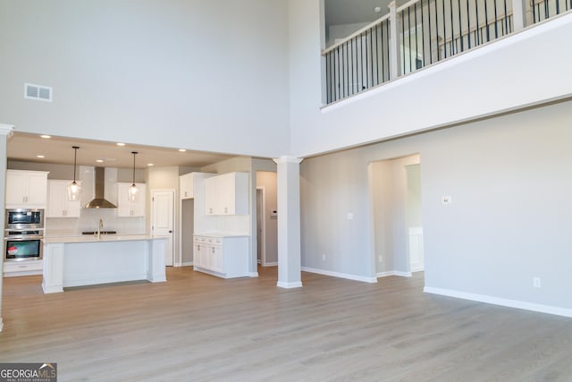 unfurnished living room featuring ornate columns, light wood-style flooring, visible vents, and a sink