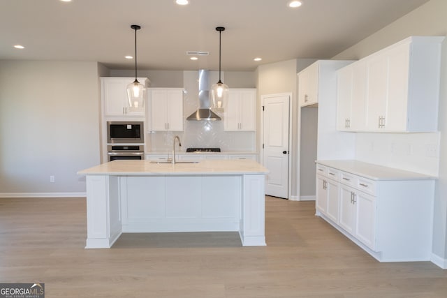 kitchen with wall chimney exhaust hood, white cabinetry, stainless steel appliances, and a sink