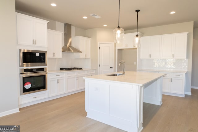 kitchen featuring light wood finished floors, visible vents, wall chimney exhaust hood, appliances with stainless steel finishes, and a sink