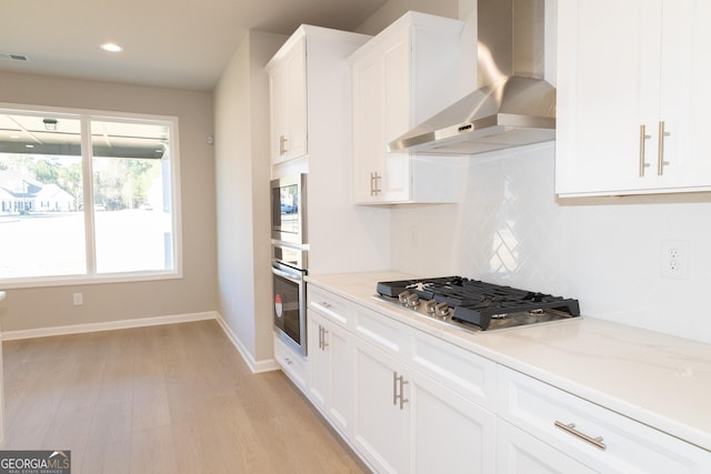 kitchen with white cabinets, wall chimney exhaust hood, stainless steel appliances, light wood-style floors, and backsplash