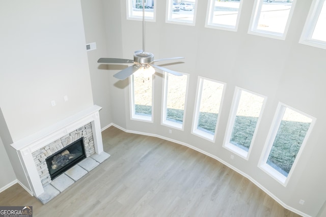 unfurnished living room featuring visible vents, a high ceiling, a stone fireplace, wood finished floors, and baseboards