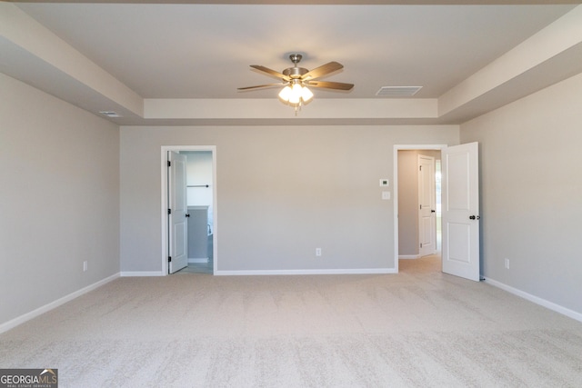 unfurnished bedroom featuring light carpet, a raised ceiling, and baseboards