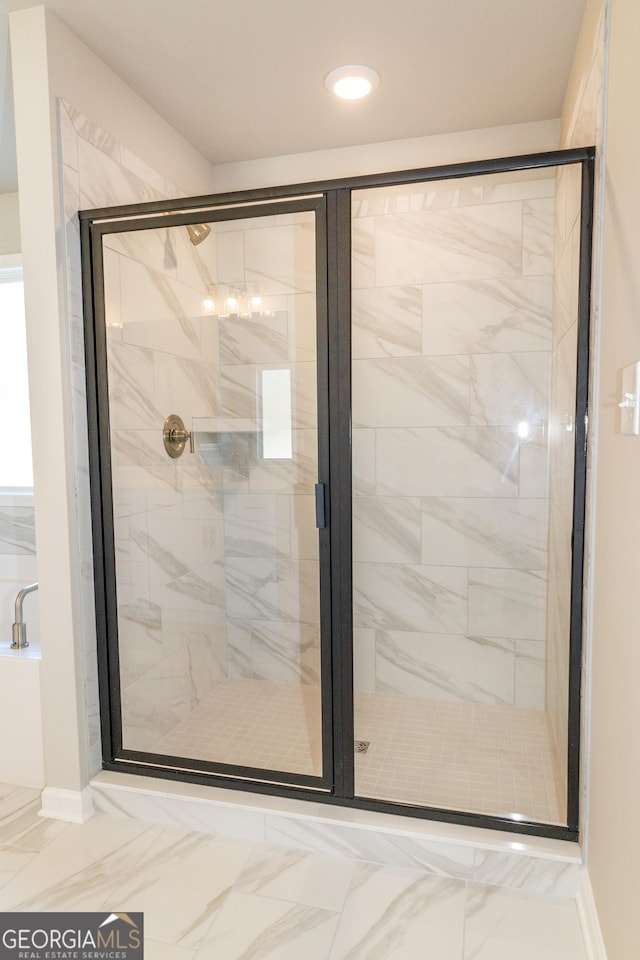 bathroom with marble finish floor, a shower stall, and baseboards