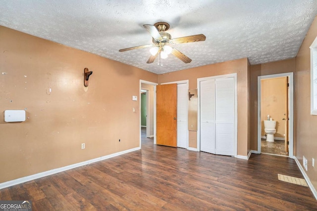 unfurnished bedroom with dark hardwood / wood-style floors, ensuite bath, ceiling fan, multiple closets, and a textured ceiling