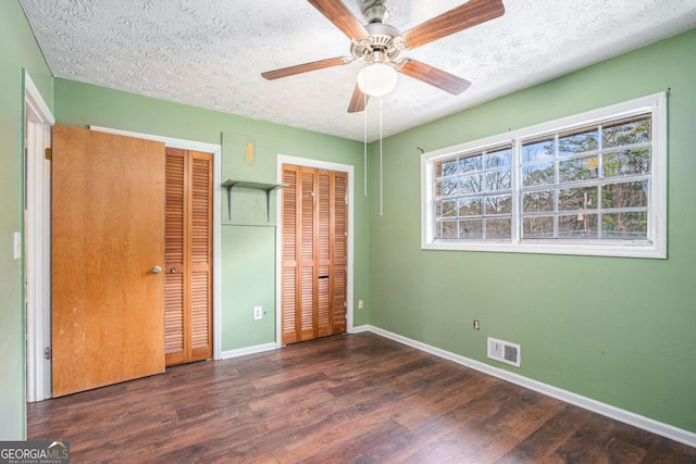 unfurnished bedroom with dark hardwood / wood-style flooring, ceiling fan, two closets, and a textured ceiling