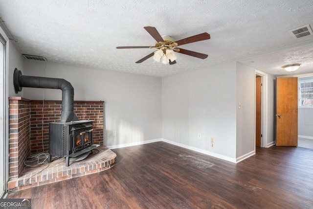 unfurnished living room with ceiling fan, a wood stove, a textured ceiling, and dark hardwood / wood-style flooring