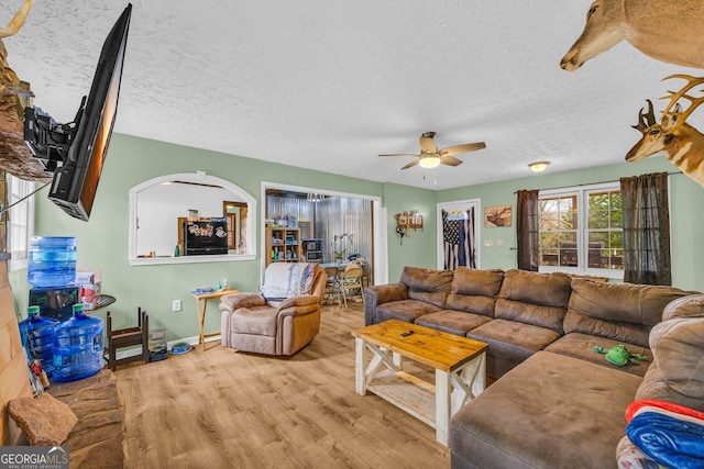 living room featuring ceiling fan, a textured ceiling, and light wood-type flooring