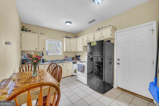 kitchen with sink, light tile patterned floors, black refrigerator, white range with electric cooktop, and cream cabinets