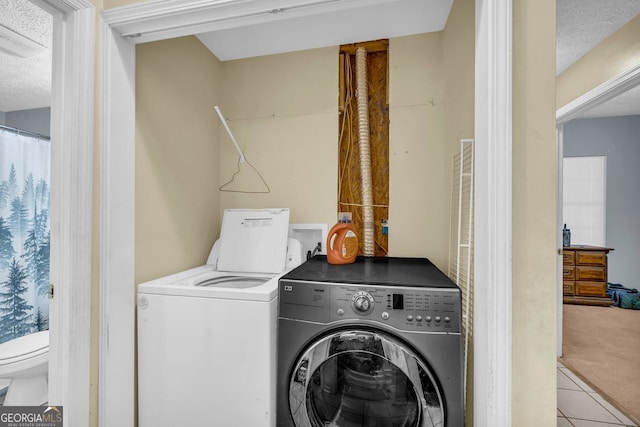 laundry area featuring washer and clothes dryer, a textured ceiling, and light tile patterned flooring