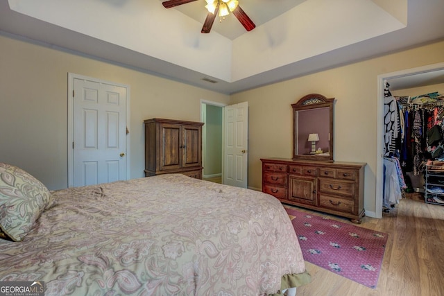 bedroom with a closet, a walk in closet, light hardwood / wood-style flooring, and a raised ceiling