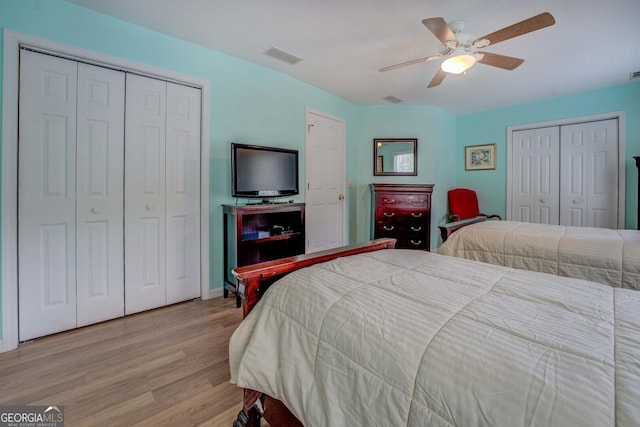 bedroom with two closets, light hardwood / wood-style floors, and ceiling fan