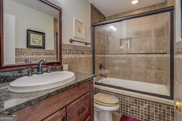 full bathroom with vanity, toilet, combined bath / shower with glass door, and tile walls