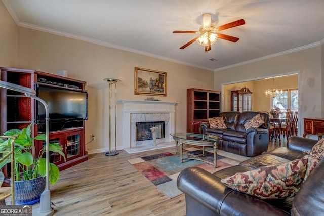 living room featuring ornamental molding, a premium fireplace, ceiling fan with notable chandelier, and light wood-type flooring