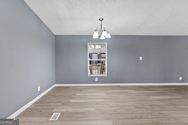 spare room with a chandelier, a textured ceiling, and light wood-type flooring