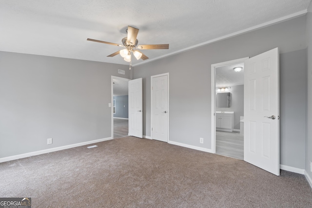 unfurnished bedroom with ceiling fan, ensuite bath, carpet flooring, and a textured ceiling