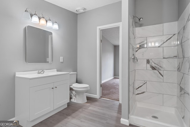 bathroom with a tile shower, vanity, wood-type flooring, a textured ceiling, and toilet