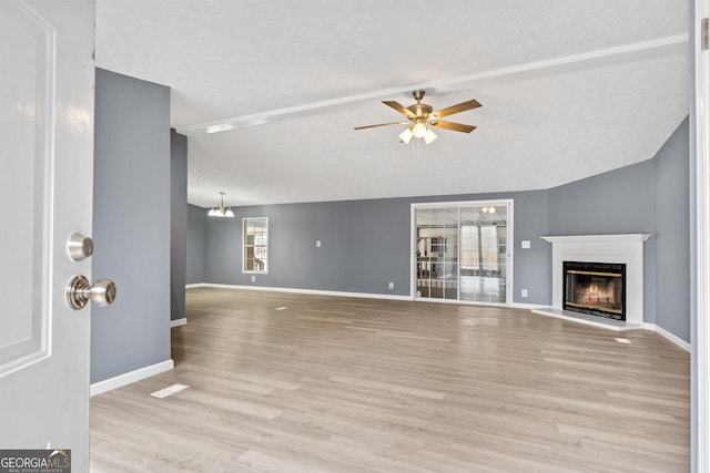 unfurnished living room with lofted ceiling, ceiling fan with notable chandelier, light hardwood / wood-style flooring, and a textured ceiling