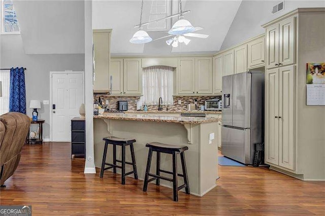 kitchen with a breakfast bar, ceiling fan, light stone counters, stainless steel refrigerator with ice dispenser, and cream cabinets