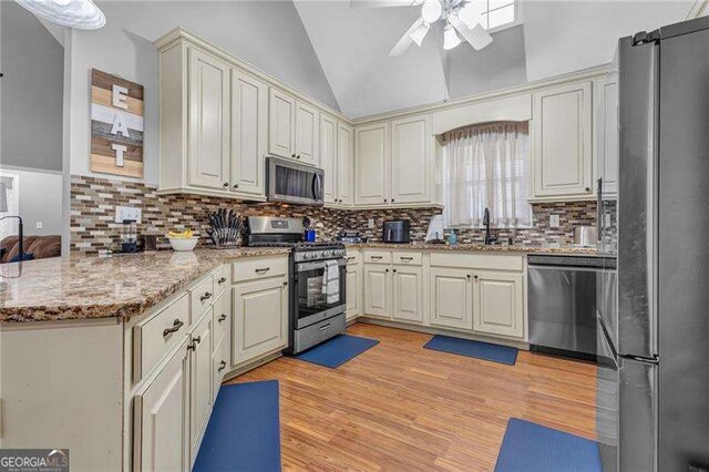 kitchen featuring appliances with stainless steel finishes, tasteful backsplash, lofted ceiling, ceiling fan, and light hardwood / wood-style flooring