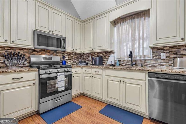 kitchen featuring tasteful backsplash, lofted ceiling, appliances with stainless steel finishes, and light hardwood / wood-style floors