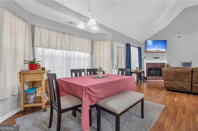 dining space featuring lofted ceiling, a fireplace, hardwood / wood-style floors, and a notable chandelier