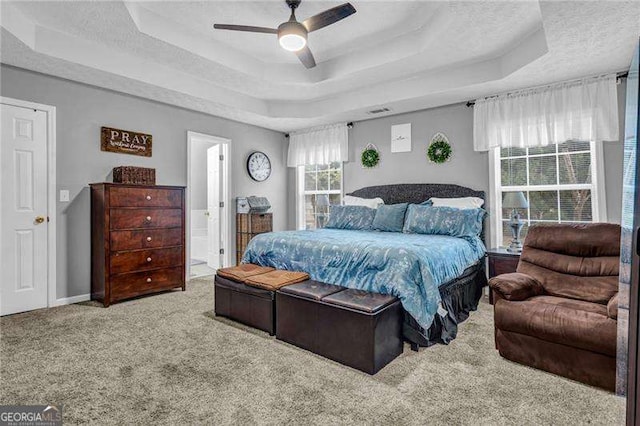 carpeted bedroom featuring a raised ceiling, ceiling fan, ensuite bathroom, and a textured ceiling