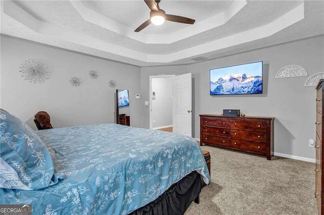 bedroom featuring a raised ceiling, light carpet, and ceiling fan