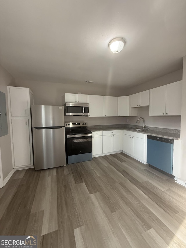 kitchen with sink, appliances with stainless steel finishes, electric panel, light hardwood / wood-style floors, and white cabinets