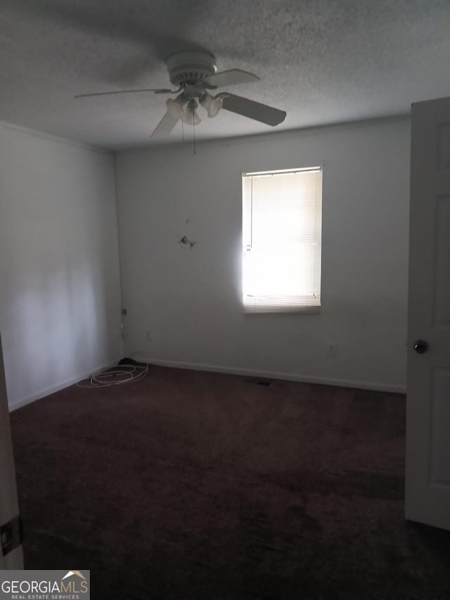 empty room with a textured ceiling, carpet flooring, a ceiling fan, and baseboards