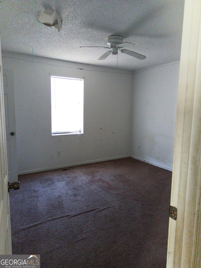 unfurnished room with a textured ceiling, dark colored carpet, a ceiling fan, and baseboards