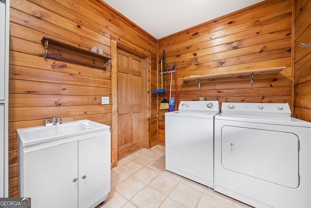 laundry room with wooden walls, washing machine and clothes dryer, light tile patterned floors, sink, and cabinets