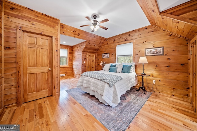 bedroom featuring light hardwood / wood-style floors, vaulted ceiling, and wooden walls