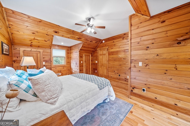 bedroom with vaulted ceiling, ceiling fan, wood walls, and light hardwood / wood-style flooring