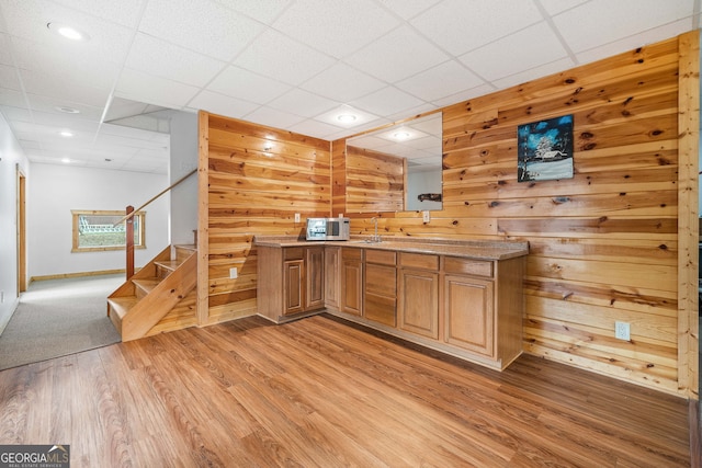 bar with light hardwood / wood-style flooring, sink, a paneled ceiling, and wood walls