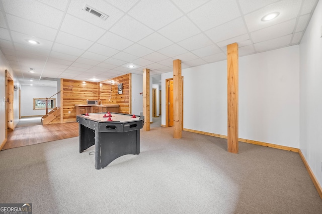 game room featuring a paneled ceiling, carpet flooring, and wood walls