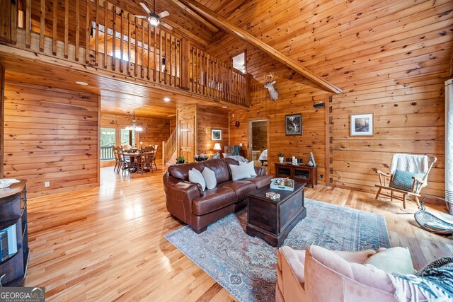 living room featuring wood walls, a high ceiling, ceiling fan, wooden ceiling, and light wood-type flooring