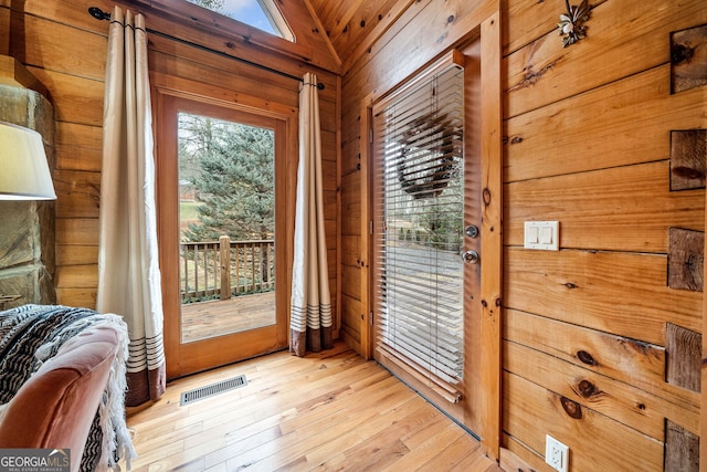 entryway featuring light hardwood / wood-style floors, lofted ceiling, wooden walls, and plenty of natural light