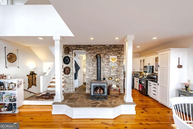 living room with wood-type flooring, decorative columns, and a wood stove