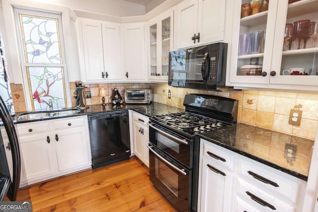 kitchen with sink, white cabinetry, dark stone countertops, black appliances, and light hardwood / wood-style floors