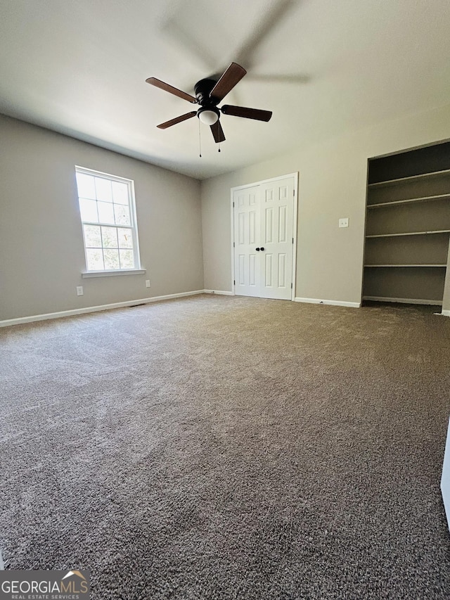 unfurnished bedroom with multiple closets, dark colored carpet, and ceiling fan