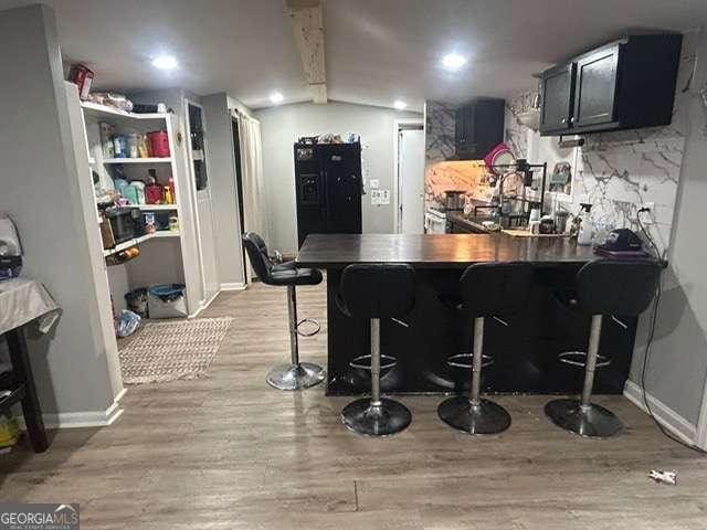 kitchen featuring a breakfast bar, vaulted ceiling with beams, decorative backsplash, kitchen peninsula, and light wood-type flooring